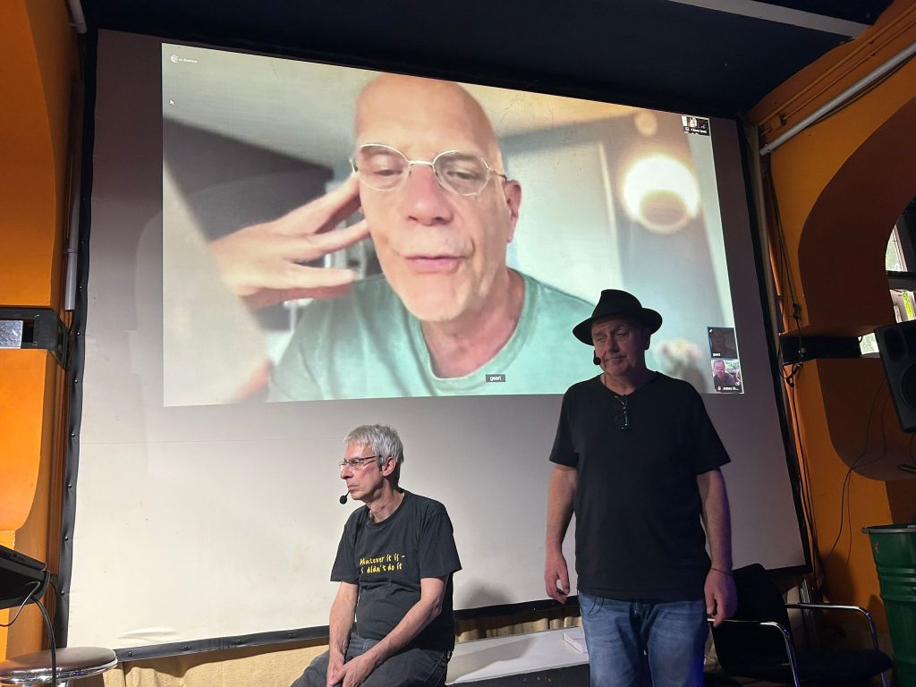 Geert Lovink on screen, Volker Grassmuck and Adam Burns in front.